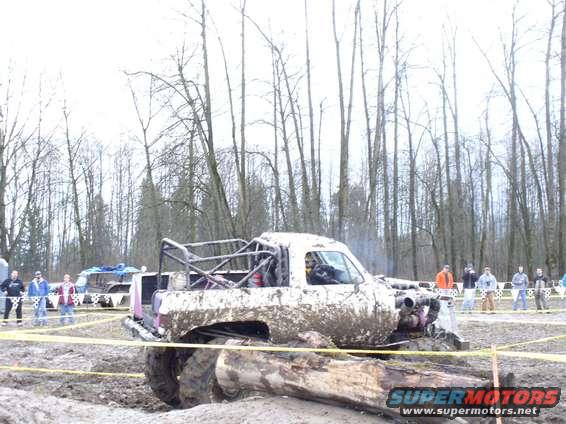 Muddy pickup truck with roll cage in a race, people watching in background