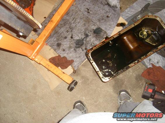 Engine oil pan with dark oil, next to an orange engine hoist on a garage floor