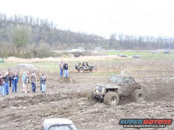 Off-road vehicles stuck in mud during a competition. People watch from the side
