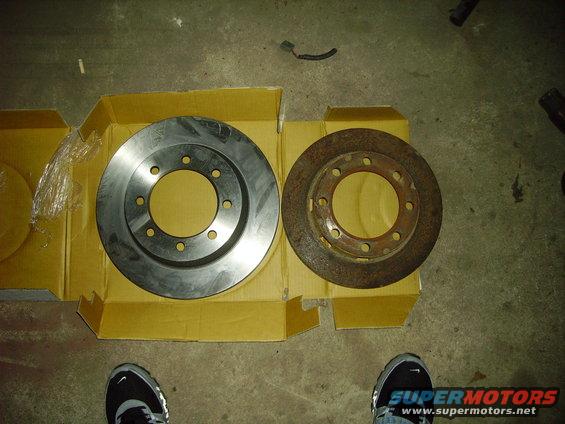 New brake rotor next to a rusty old one, both in a cardboard box
