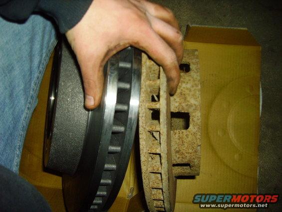 Hand holding new brake rotor next to heavily rusted old brake rotor