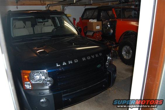 Front of a dark blue Land Rover Discovery parked in a garage next to an orange off-road vehicle
