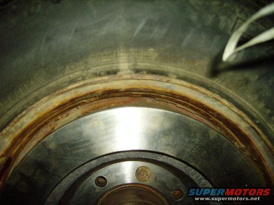 Close-up of a rusty brake rotor with visible wear marks. Text on the tire is partially legible
