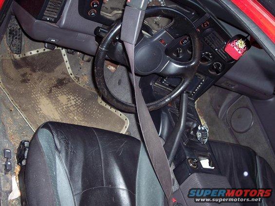 Interior of a 1991 Mitsubishi Eclipse, showing black leather seats, a worn steering wheel, and a dirty floor mat