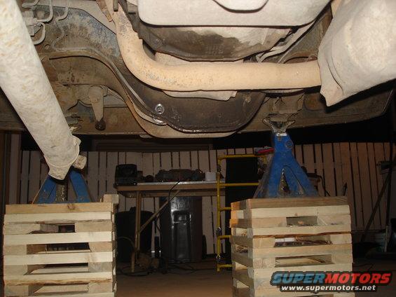 Underside of a vehicle on jack stands, showing exhaust and suspension components