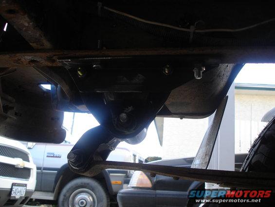 Underside of a vehicle with suspension components and a tire visible; other vehicles in background