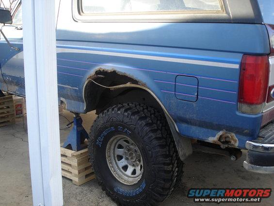 Blue 1990 Ford Bronco rear quarter panel with rust around the wheel well and a gas cap door