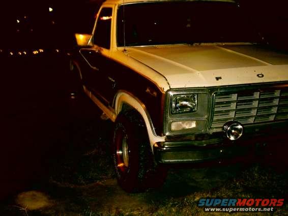 Front view of a white and maroon Ford F-Series truck at night. It has a chrome grille and a round fog light