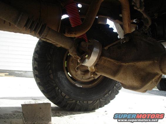Undercarriage view of a vehicle's rear axle and driveshaft, with a red shock absorber visible