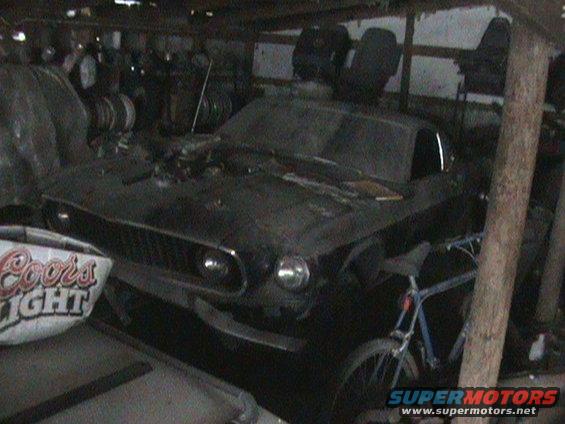 old car with a grille that looks like a 1969 Mustang, parked inside a cluttered garage with a bike and some seats
