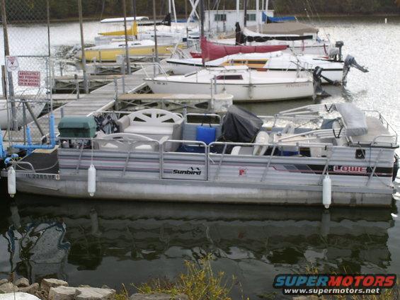 Pontoon boat docked at a marina with other boats in the background. License plate reads IL 2265 HE