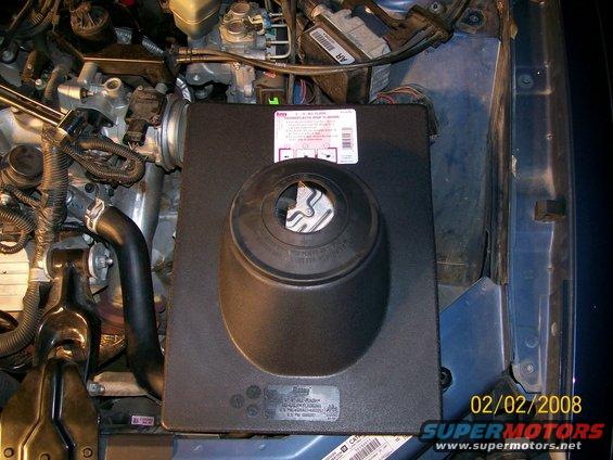 Engine compartment showing air intake assembly and hoses. Label visible on assembly