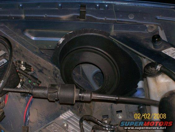 Close-up of engine bay with hoses, wires, and a black circular component