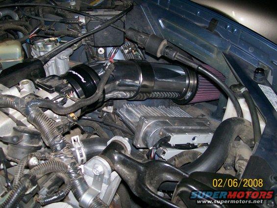 Engine bay with shiny intake tube and red air filter. ECU visible