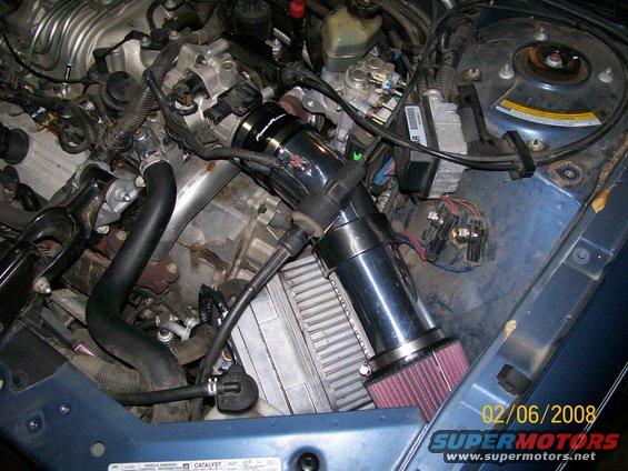 Engine compartment with aftermarket air intake, hoses, and wiring. Blue painted metal visible