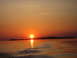1996 Dodge 2500 - The sun sets over a calm body of water, casting an orange glow on the sky and reflecting on the gentle waves.