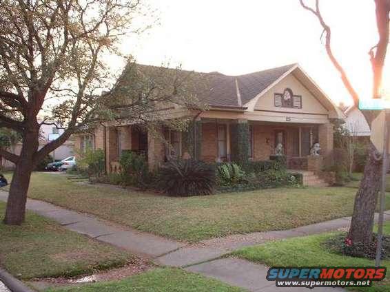 Front view of a brick house with a porch and a large tree in the yard