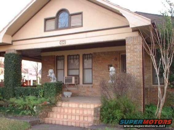 Front porch of a house with brick columns, stairs, and landscaping. There are two lion statues