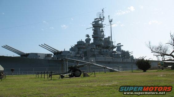 Battleship USS North Carolina with a cannon in the foreground, grassy field, and blue sky