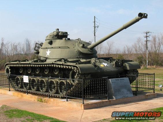 Olive drab tank with white star insignia and long barrel, displayed behind a fence