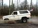 1980 Ford Bronco - White 1980 Ford Bronco kicks up mud while driving off-road with American flags attached.