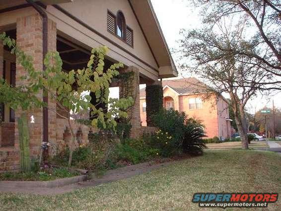 Front porch of a brick house with a tree in the yard. A street and another house are visible in the background