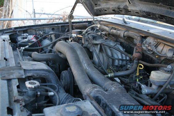 Engine bay of a 1990 Ford Bronco, showing the V8 engine with hoses and battery