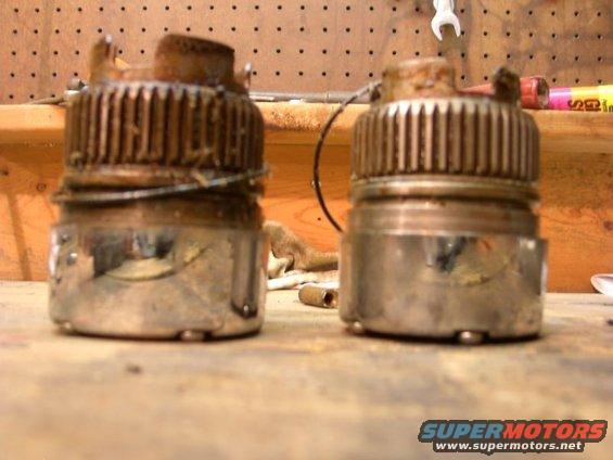 Two rusty, cylindrical automotive parts with ribbed tops sit side-by-side on a workbench