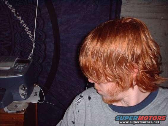 Person with red hair and beard, wearing a grey t-shirt with black marks