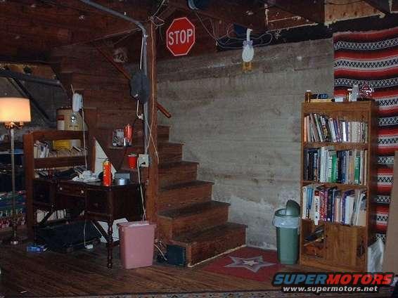 Basement room with wooden stairs, a desk, a bookshelf, and a stop sign
