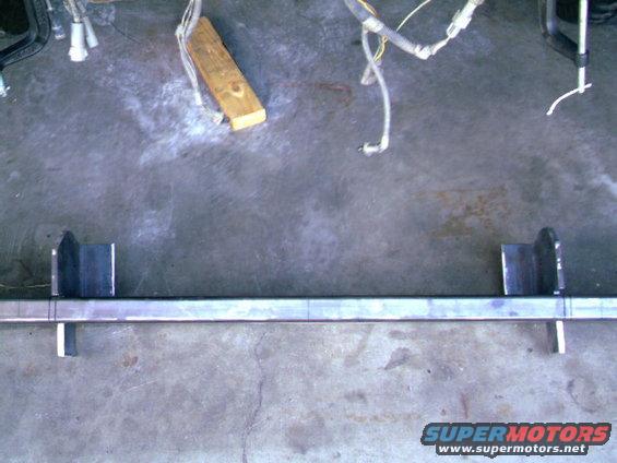 Metal bar with brackets welded on, ready for bumper fabrication. Wires and wood block nearby