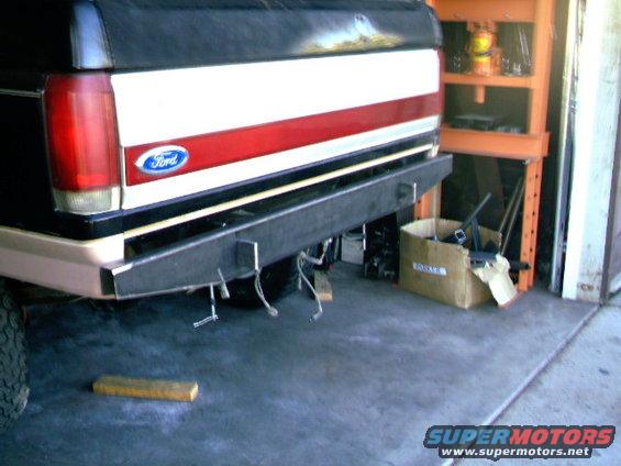 Rear of a Ford truck with a custom bumper installed. Has a red and white stripe on the tailgate