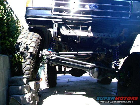 1989 Ford Bronco front suspension with large off-road tire on blocks. Ford grille visible
