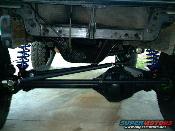 Undercarriage of a vehicle with blue coilover shocks, a large differential, and a Supermotors.net watermark
