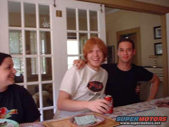 Three people smiling at a table with a red can and a plate of crackers