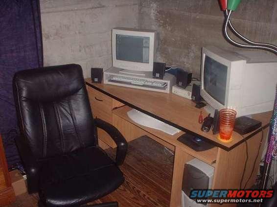 Office desk with two computer monitors, keyboard, speakers, and a black leather chair