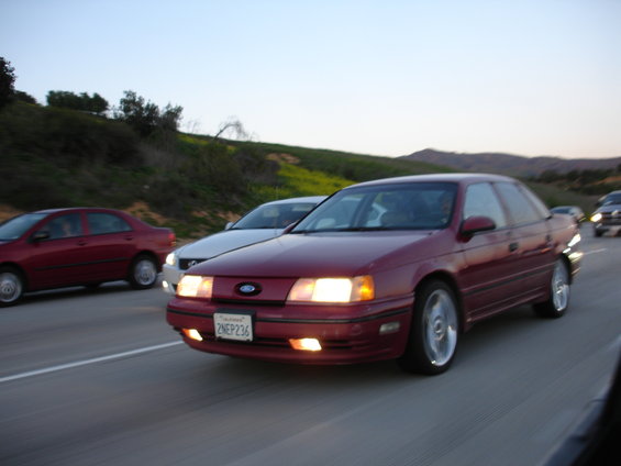 Maroon 1991 Ford Taurus driving on highway, front view. License plate 2NEP236