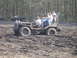 1989 Ford Bronco - Several people ride in a custom off-road vehicle as it navigates a muddy terrain, with other ATVs in the distance.