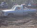 1989 Ford Bronco - A blue GMC pickup truck is stuck deep in the mud, with several people observing the scene.