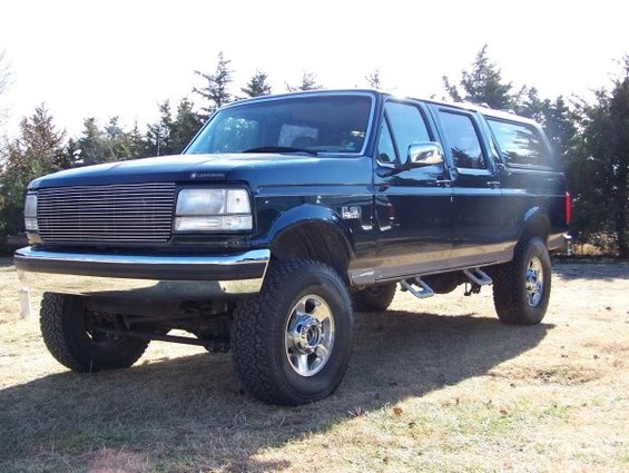 Dark blue Ford Bronco Centurion conversion with aftermarket grille and running boards, parked on grass