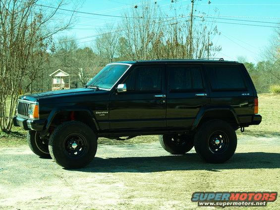Black Jeep Cherokee with lifted suspension and aftermarket wheels parked on a dirt lot