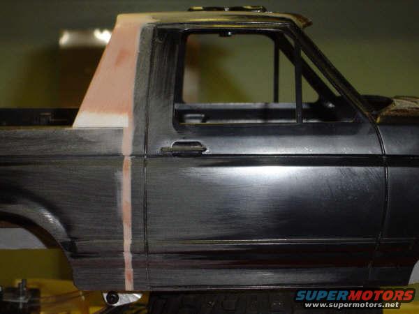 Side view of a dark gray 1992 Ford Bronco body with primer on the rear pillar