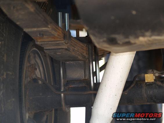 Leaf spring suspension with U-bolts and a white shock absorber. Rusty metal components are visible