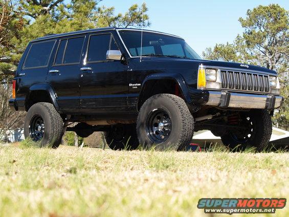 Black Jeep Cherokee with lifted suspension and off-road tires, viewed from a low angle