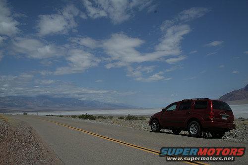 Red SUV parked on desert roadside under a cloudy blue sky