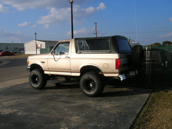 Tan Ford Bronco with a soft top and spare tire on the rear, parked on asphalt