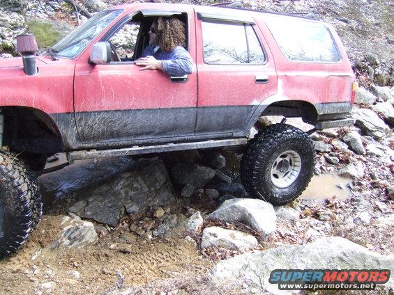 Red SUV with black trim and large tires navigating rocky terrain