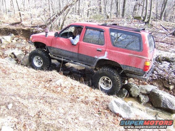Red SUV with large tires off-roading through a creek bed