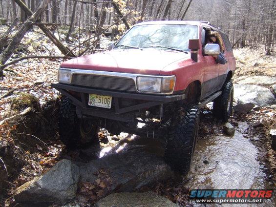Red Toyota 4Runner with lifted suspension and off-road tires driving through a rocky stream