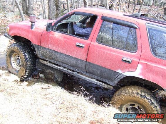 Red SUV with large tires stuck in mud on a wooded trail. Snorkel intake visible